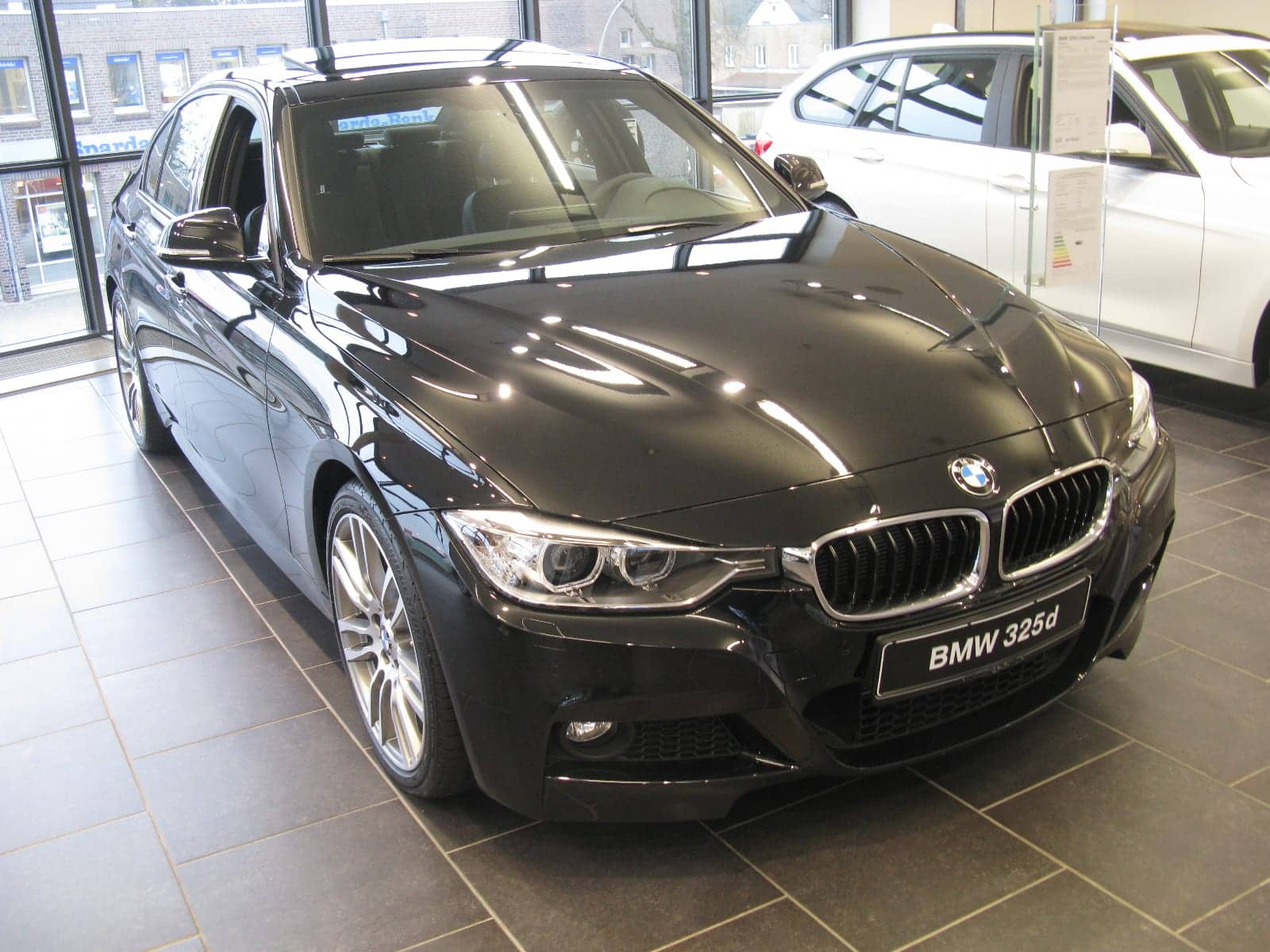 Black BMW 325d M Sport sedan in a showroom, front three-quarter view