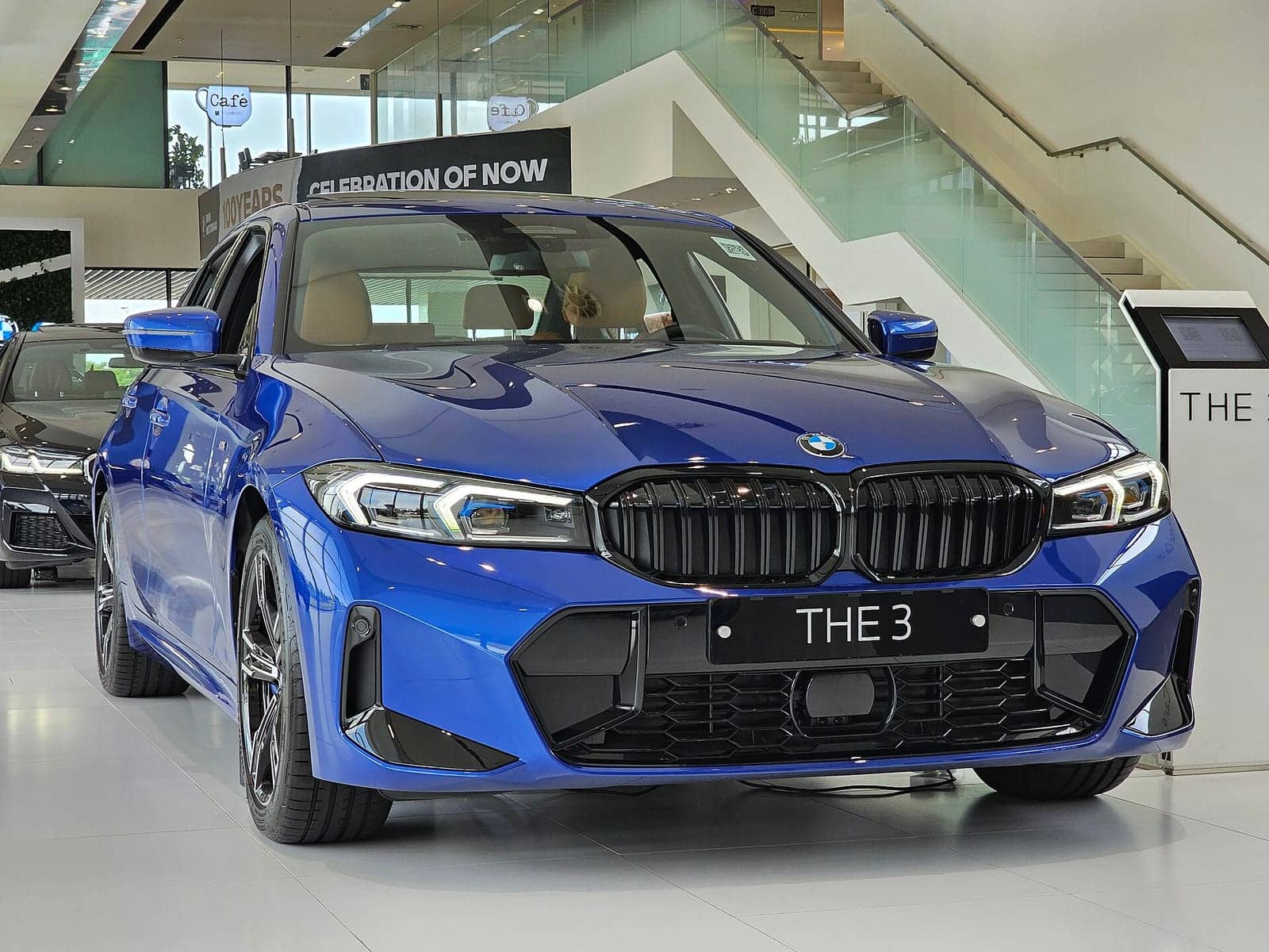 Blue BMW 320i M Sport sedan in a showroom, front three-quarter view