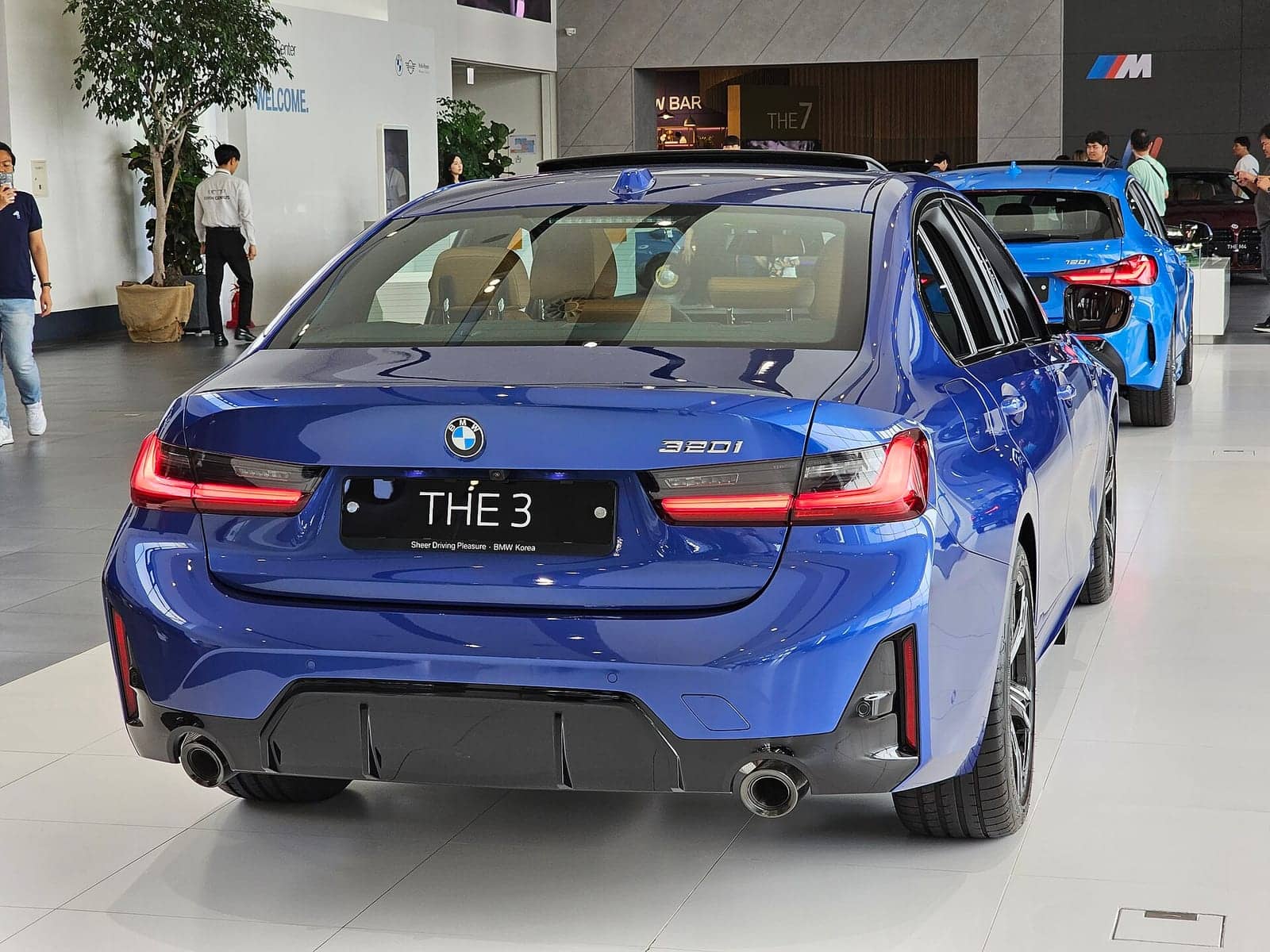 Blue BMW 320i M Sport sedan in a showroom, rear view