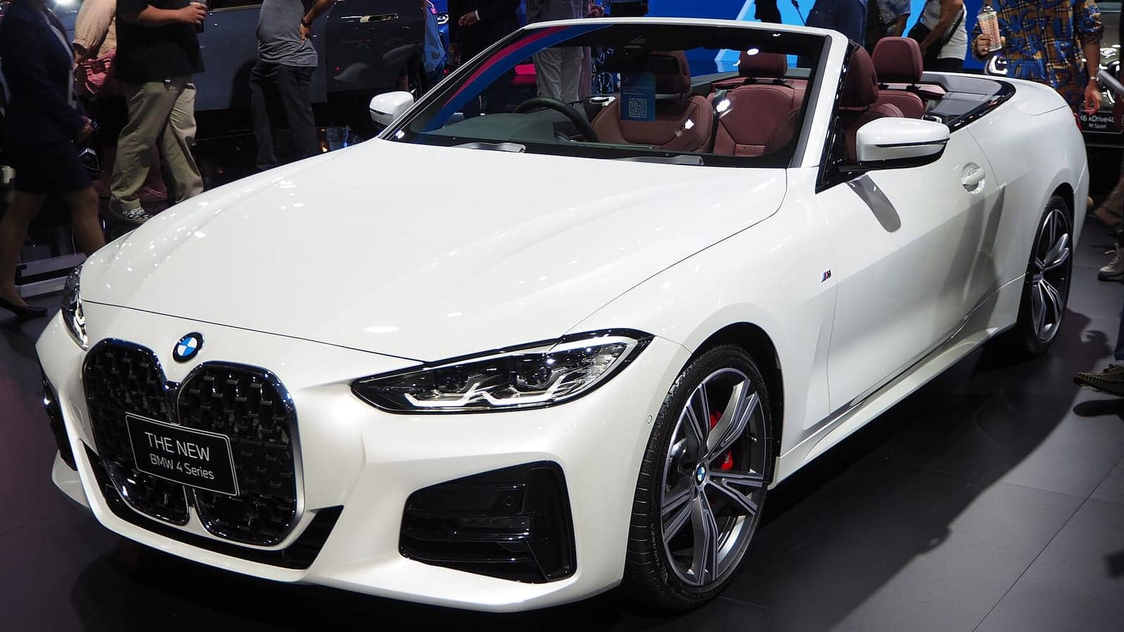 White BMW 430i M Sport convertible with the top down at a motor show, front three-quarter view