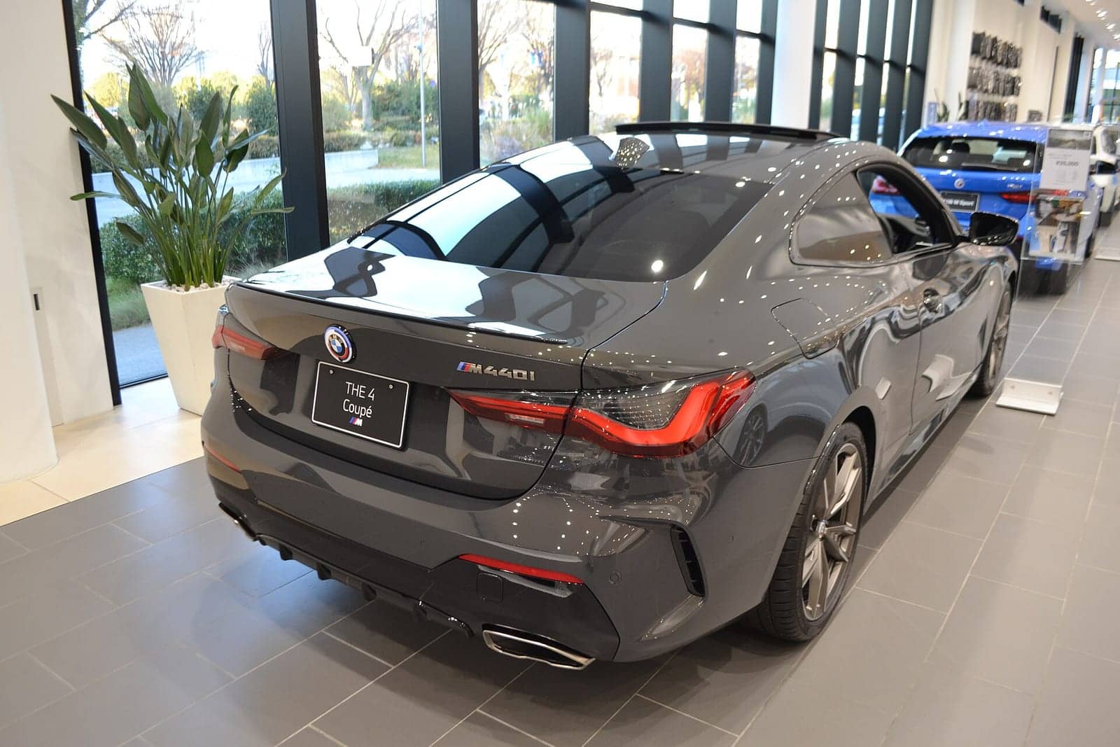 Grey BMW M440i xDrive coupé in a showroom, rear three-quarter view