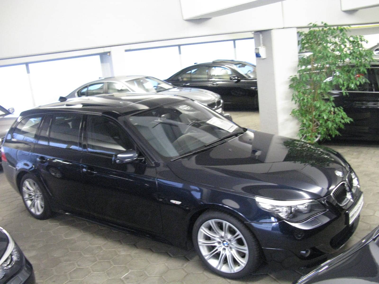 Dark blue BMW 550i Touring M Sport in a showroom, front three-quarter view