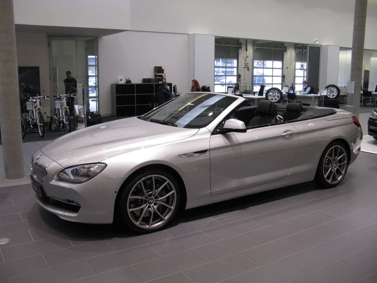 Silver BMW 640i convertible with the top down in a showroom, front three-quarter view
