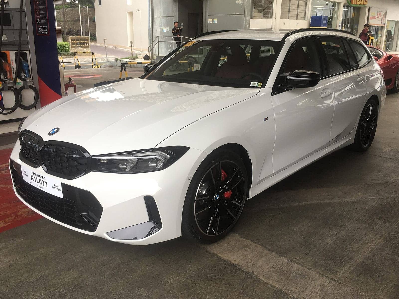 White BMW M340i xDrive Touring in a showroom, front three-quarter view